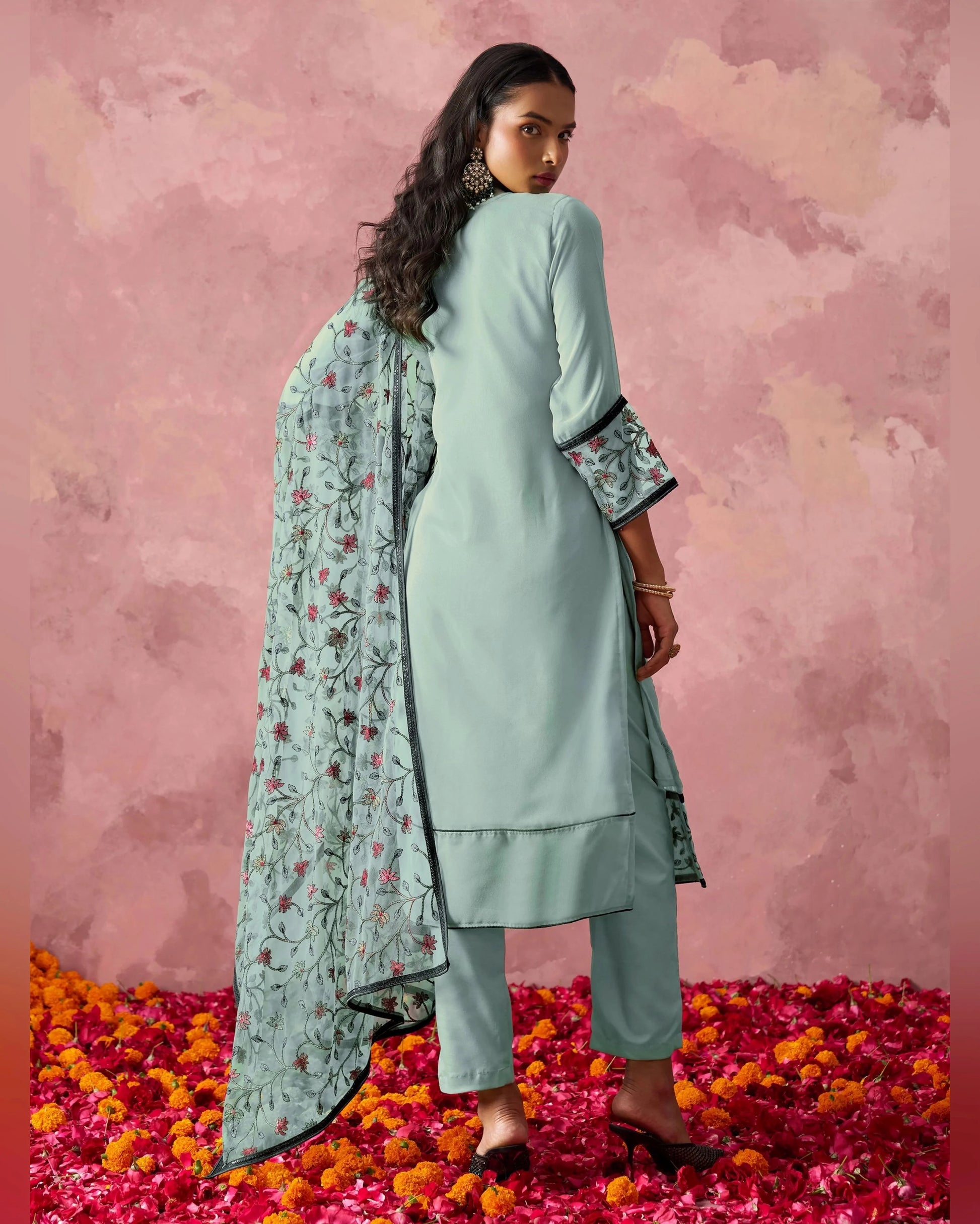 Woman in a light blue traditional outfit with a floral dupatta on a pink floral background