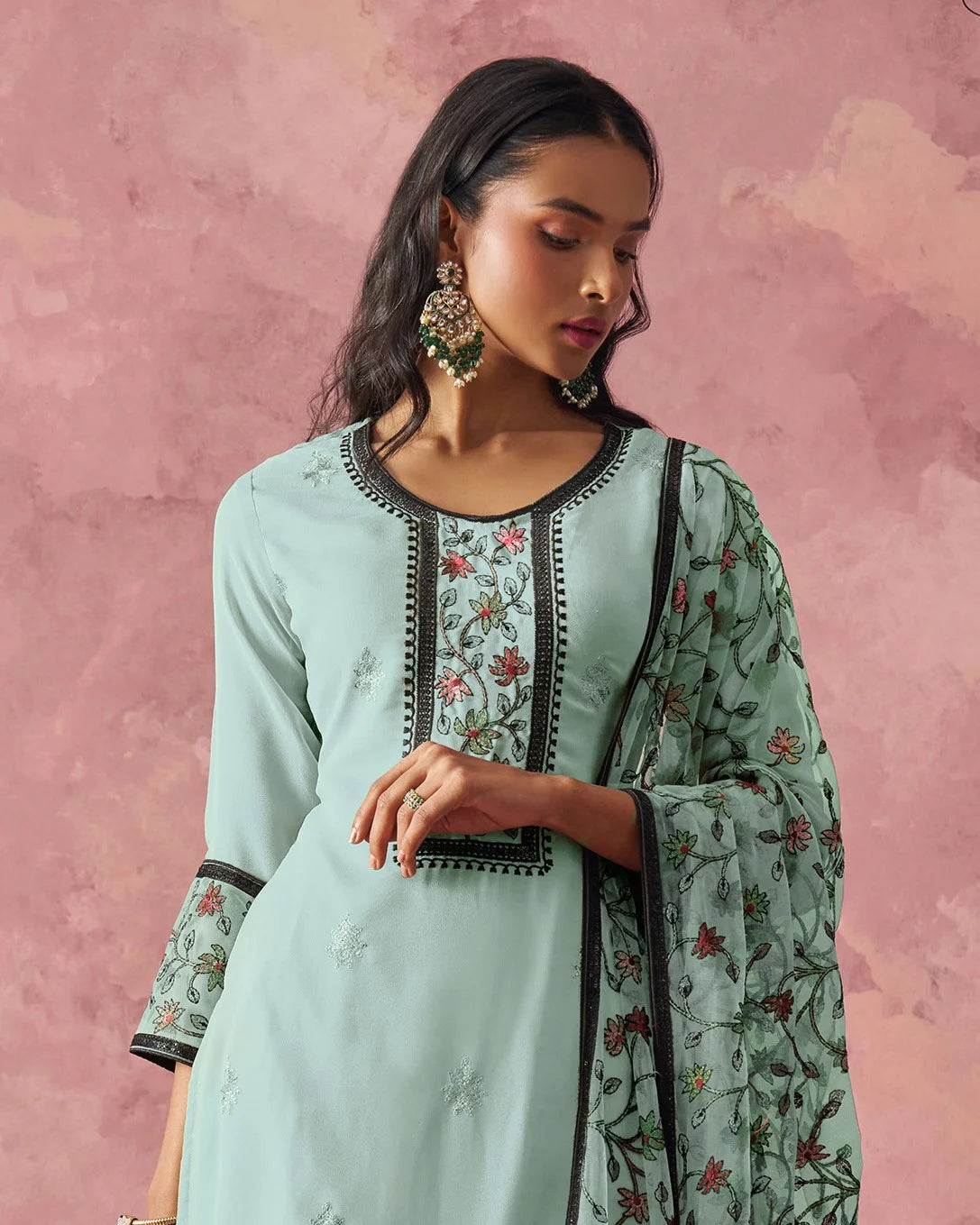 Woman wearing a light blue traditional outfit with floral patterns against a pink background