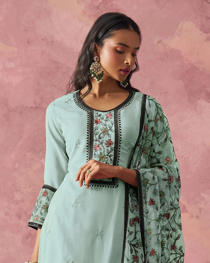 Woman wearing a light blue traditional outfit with floral patterns against a pink background