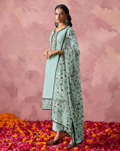 Woman in a light blue traditional outfit with floral patterns on a pink background with flower petals.