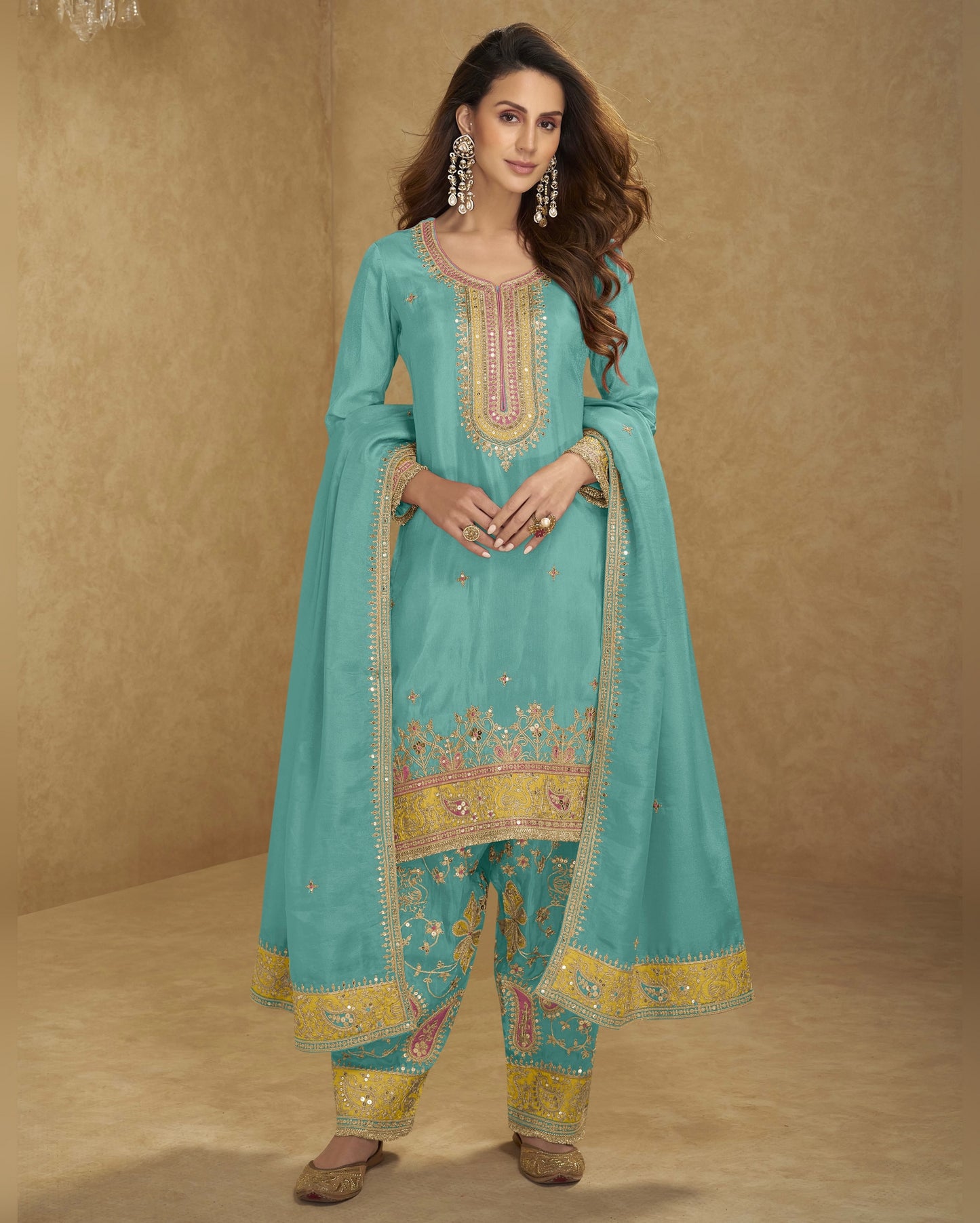 Woman wearing a turquoise embroidered traditional outfit on a beige background