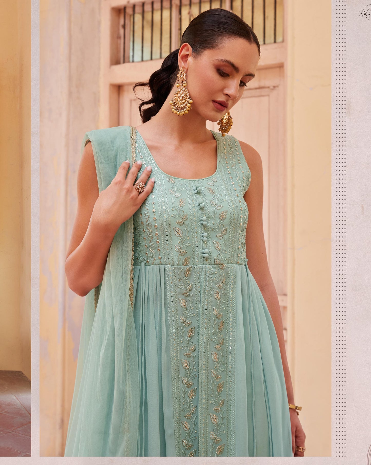Woman wearing a light blue embroidered dress with gold details indoors.