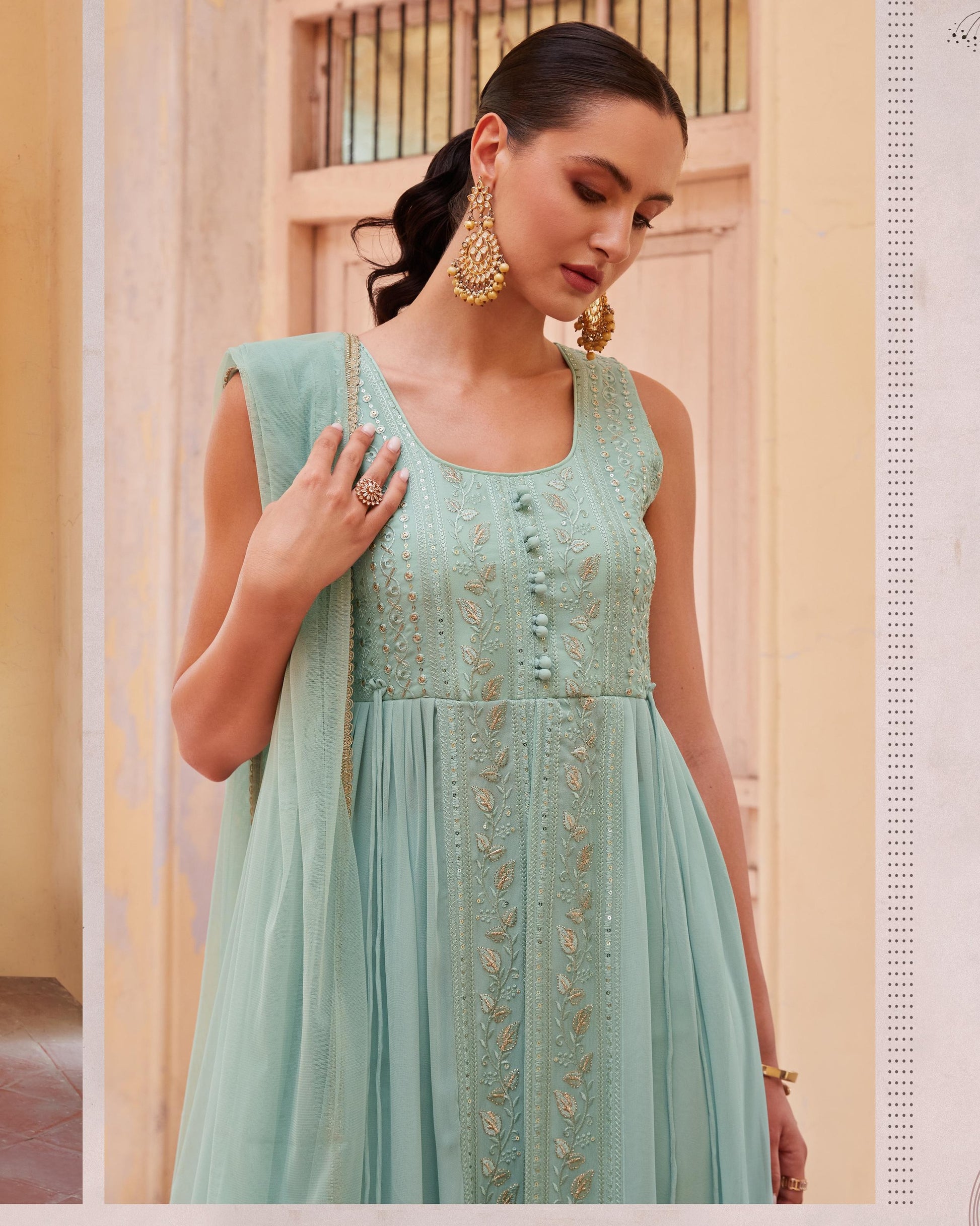 Woman wearing a light blue embroidered dress with gold details indoors.