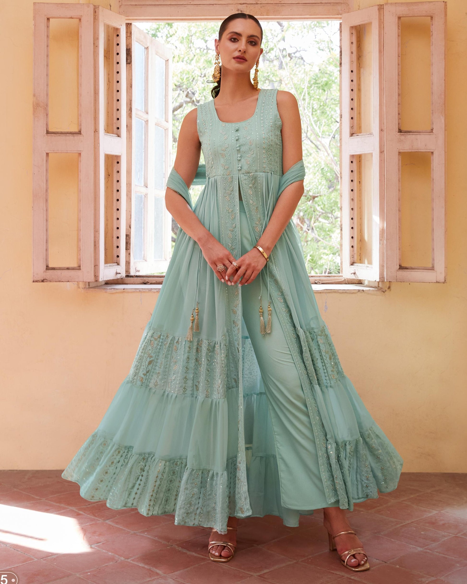 Woman wearing a light blue dress with lace details in a room with open shutters.