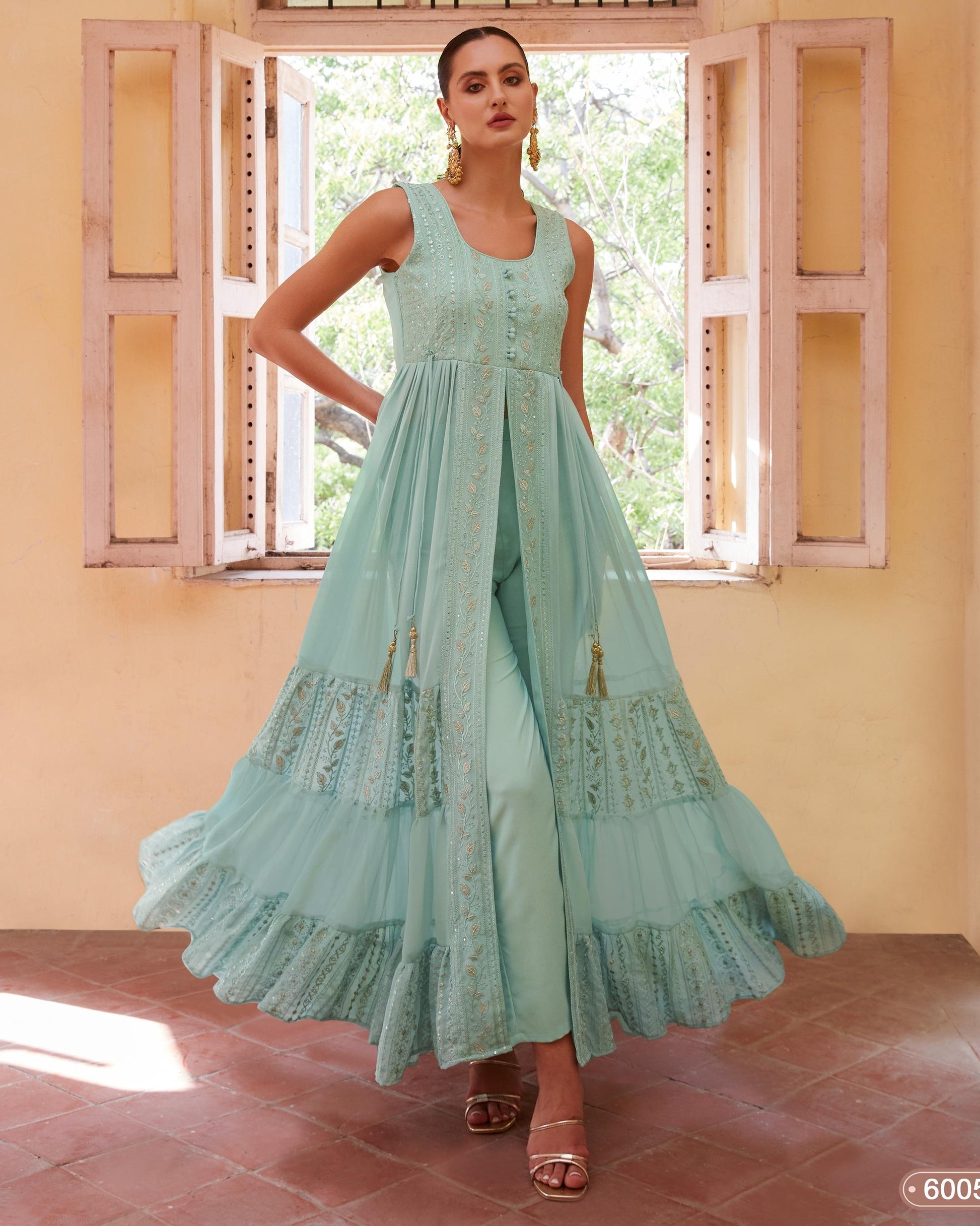 Woman wearing a light blue embroidered dress standing in front of a window with a pink wall.