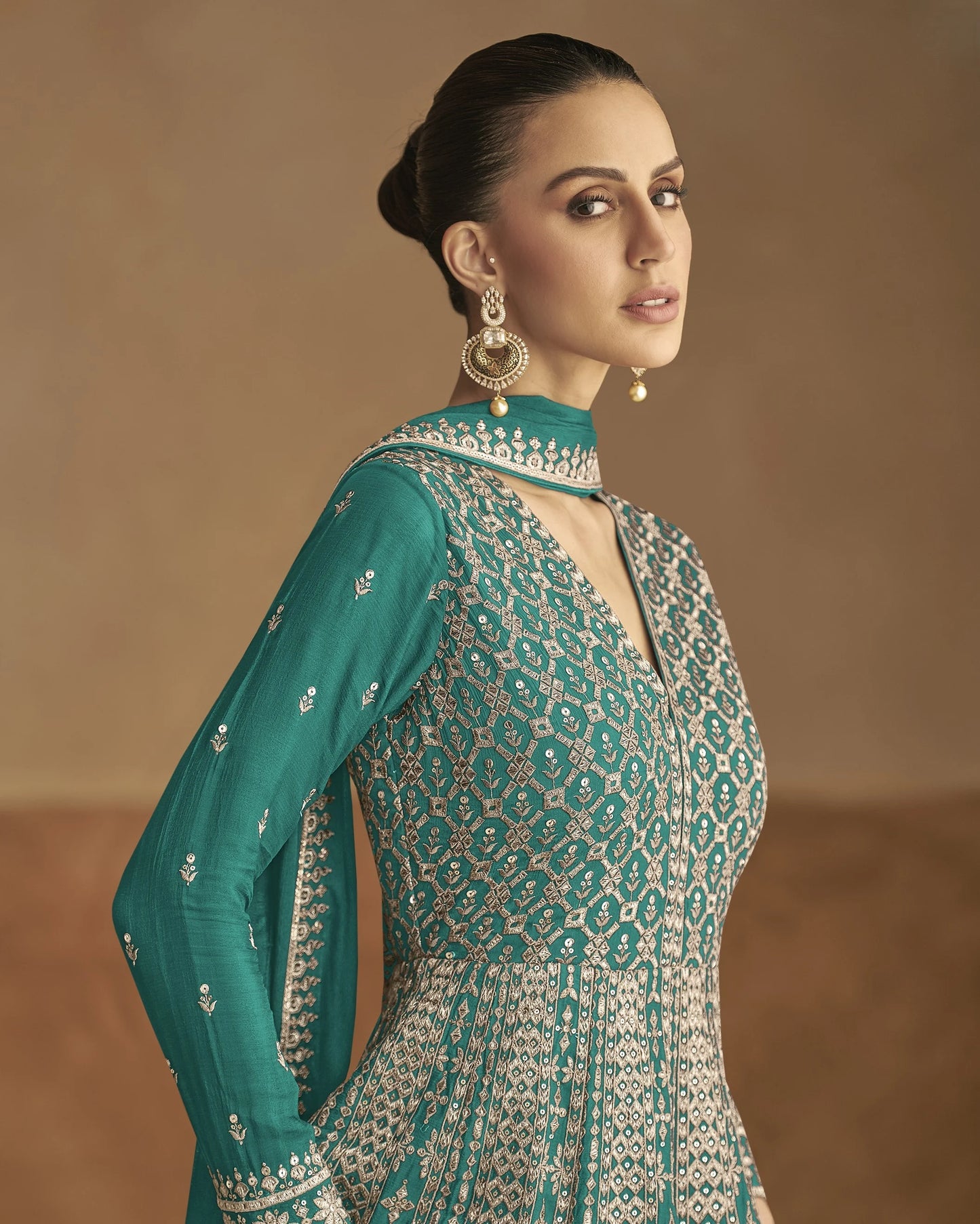 Woman wearing a teal and patterned outfit with gold jewelry against a beige background