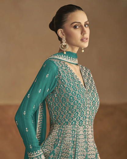 Woman wearing a teal and patterned outfit with gold jewelry against a beige background