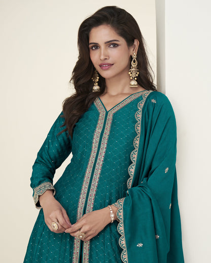 Woman wearing a teal traditional outfit with gold embroidery on a beige background