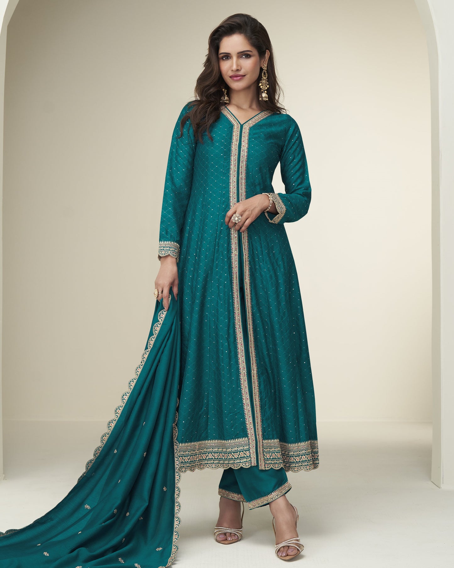 Woman wearing a teal traditional outfit with gold embroidery on a neutral background