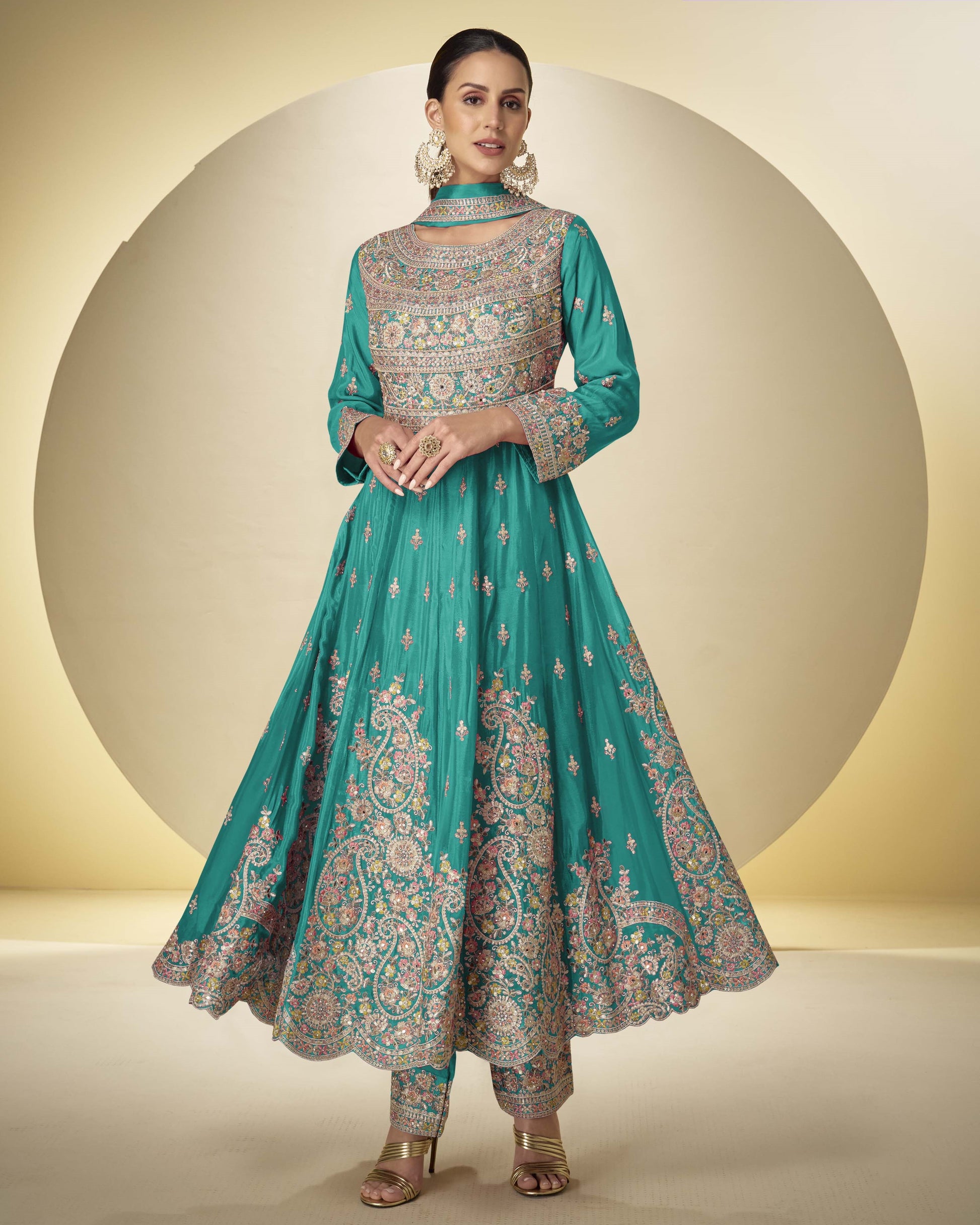 Woman wearing a teal embroidered traditional outfit on a beige background