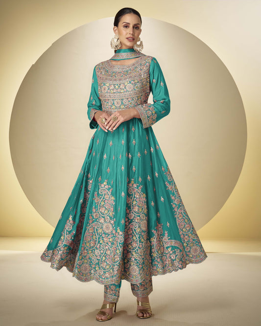 Woman wearing a teal embroidered traditional outfit on a beige background