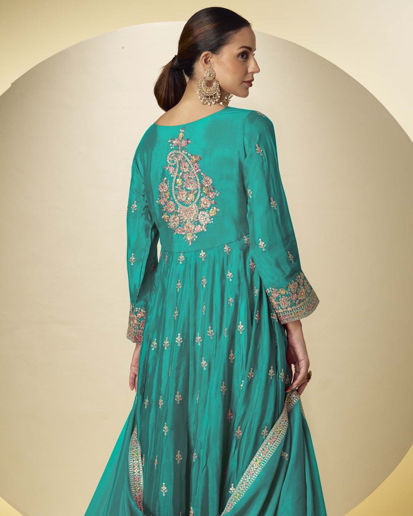 Woman wearing a teal embroidered dress against a beige background