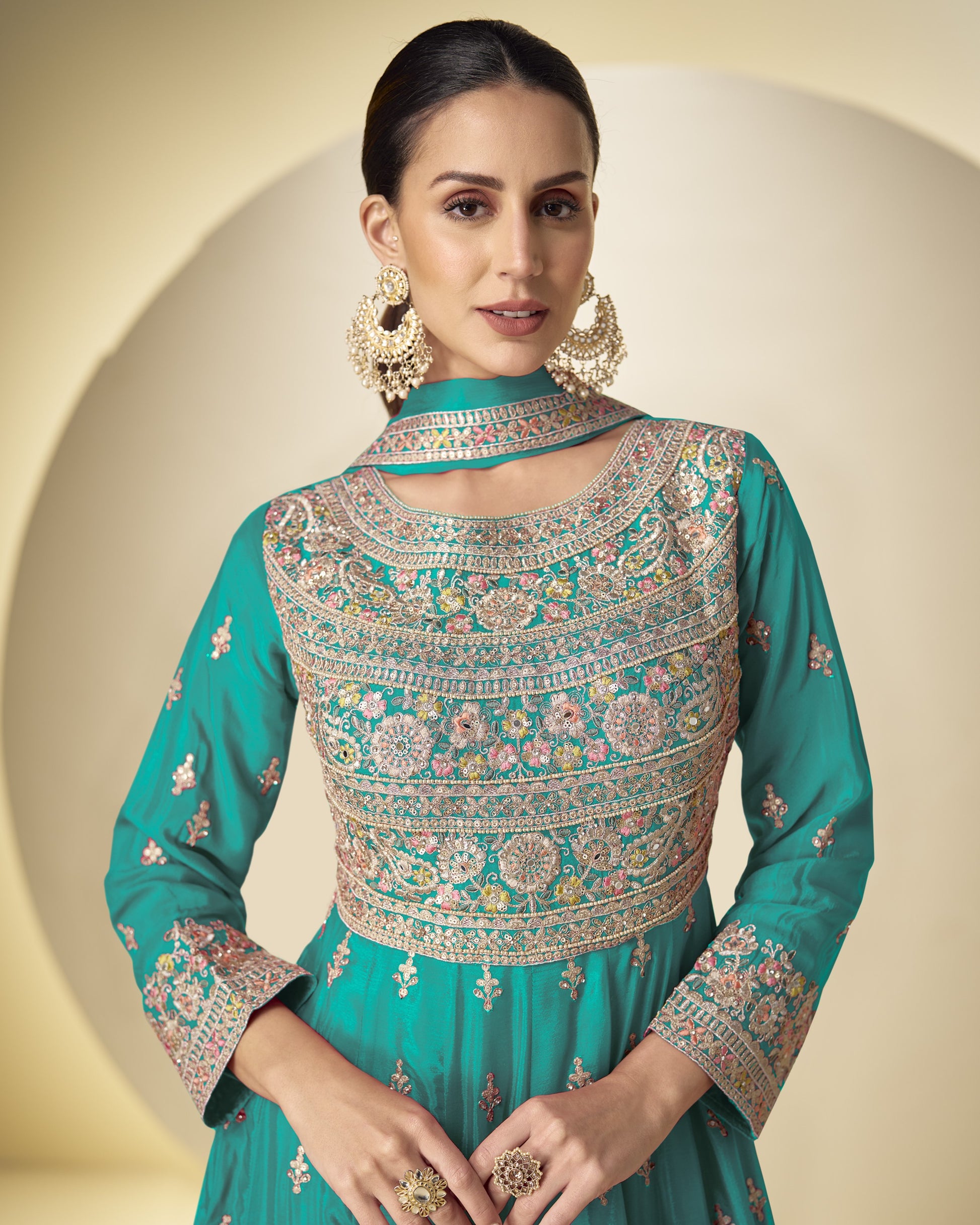 Woman wearing a teal embroidered traditional outfit with a beige background