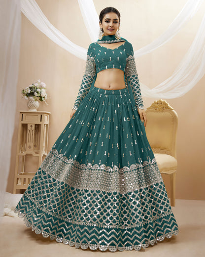 Woman wearing a teal embroidered lehenga with a beige background