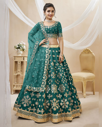 Woman wearing a teal embroidered traditional outfit in a decorated room.