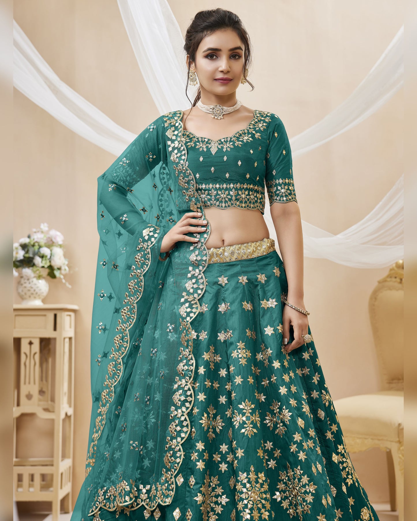 Woman wearing a green embroidered traditional outfit with gold details in an elegant indoor setting.