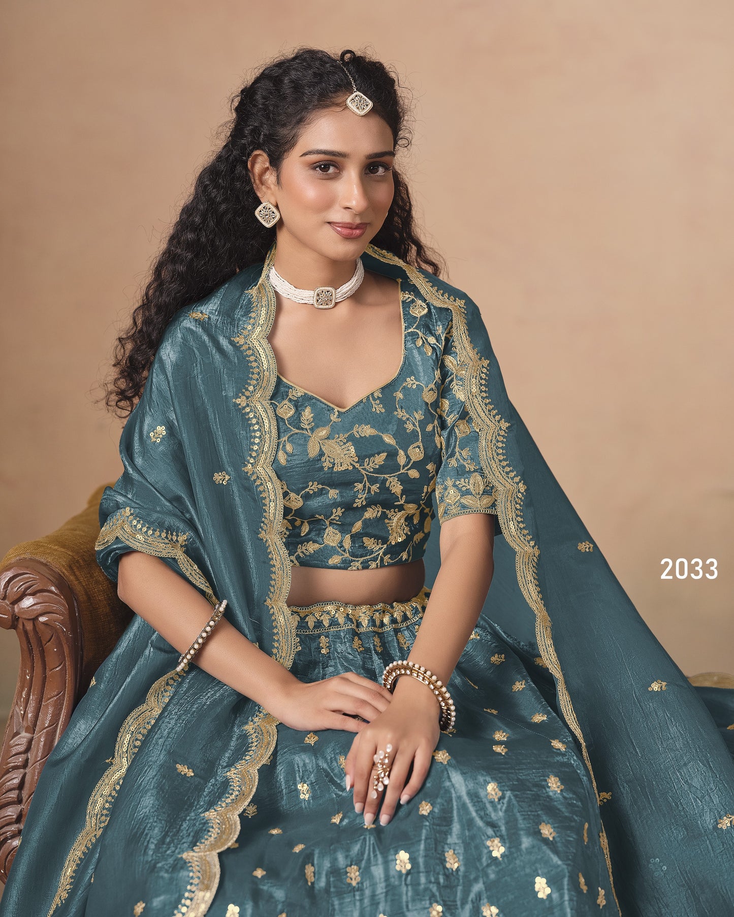Woman in a teal traditional outfit with gold embroidery on a beige background