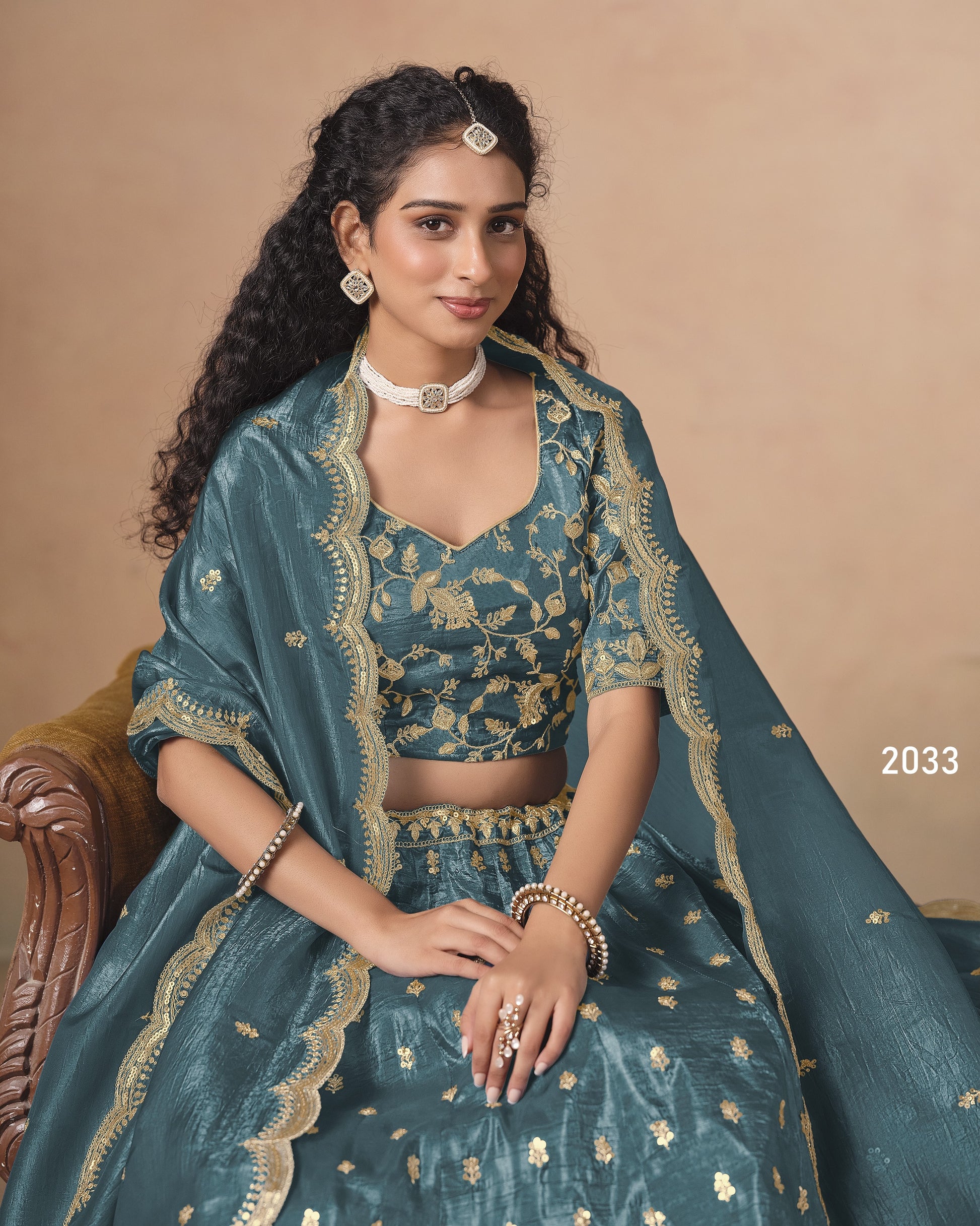 Woman in a teal traditional outfit with gold embroidery on a beige background