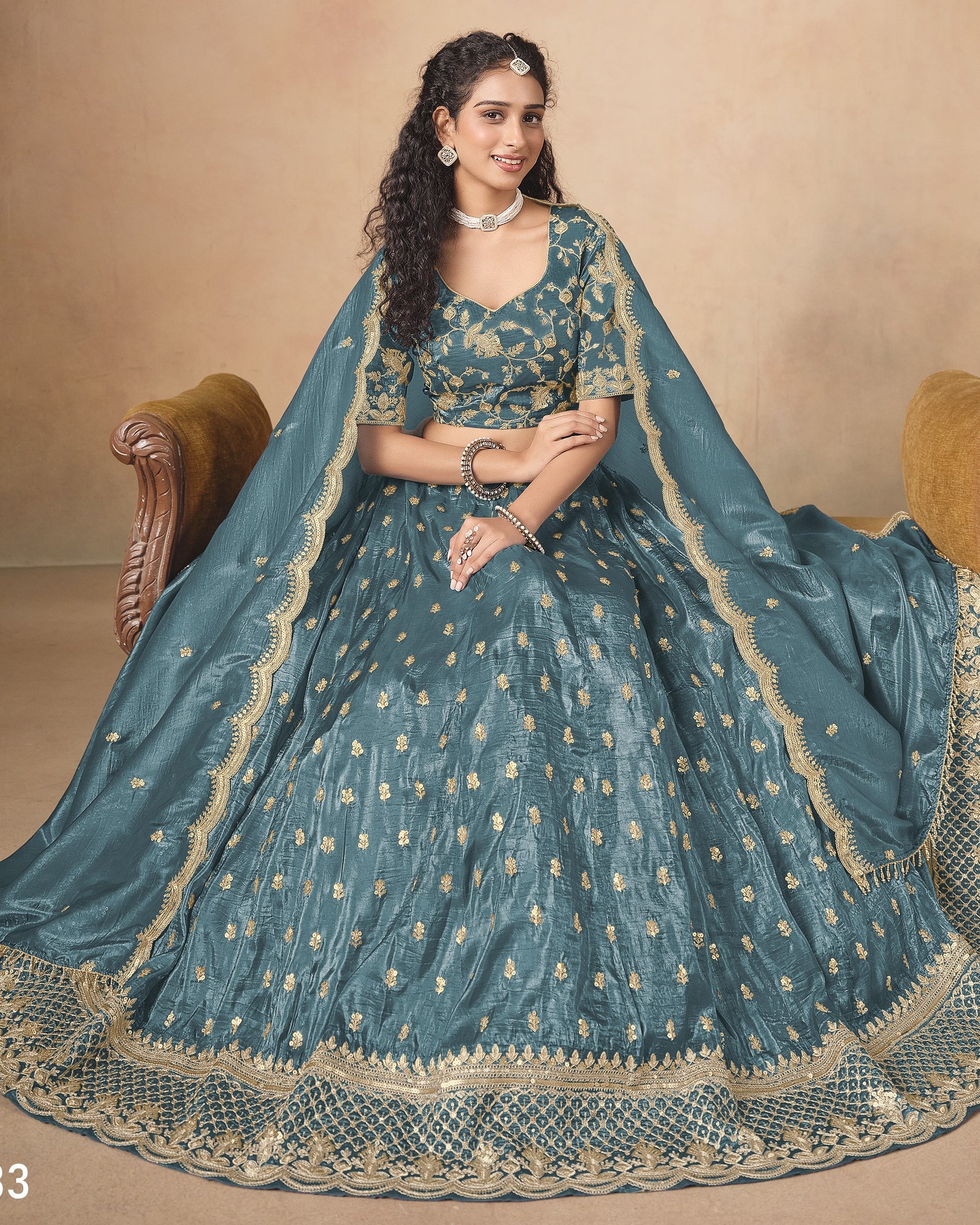 Woman wearing a traditional teal and gold embroidered outfit on a beige background