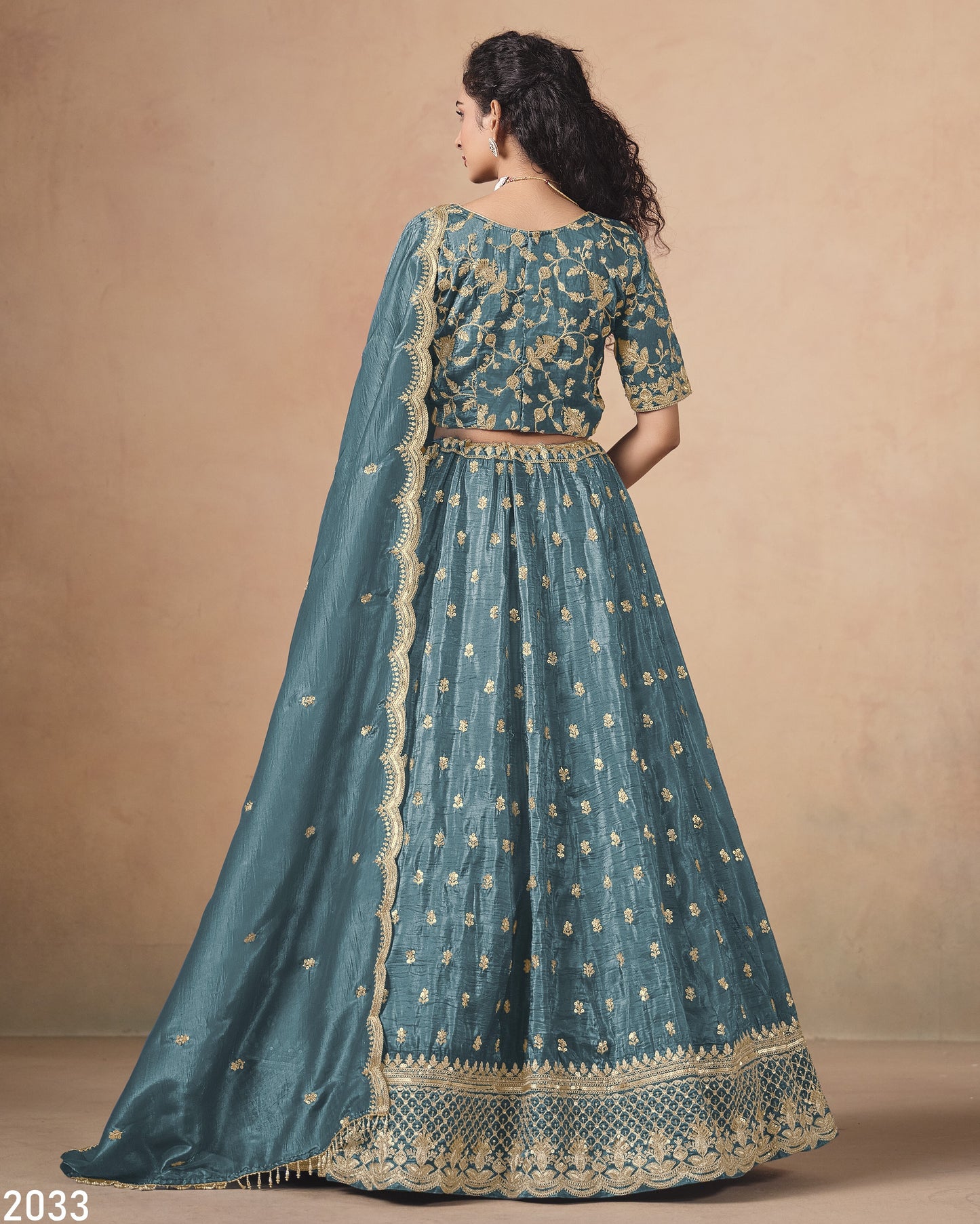 Teal embroidered traditional outfit with gold details on a beige background