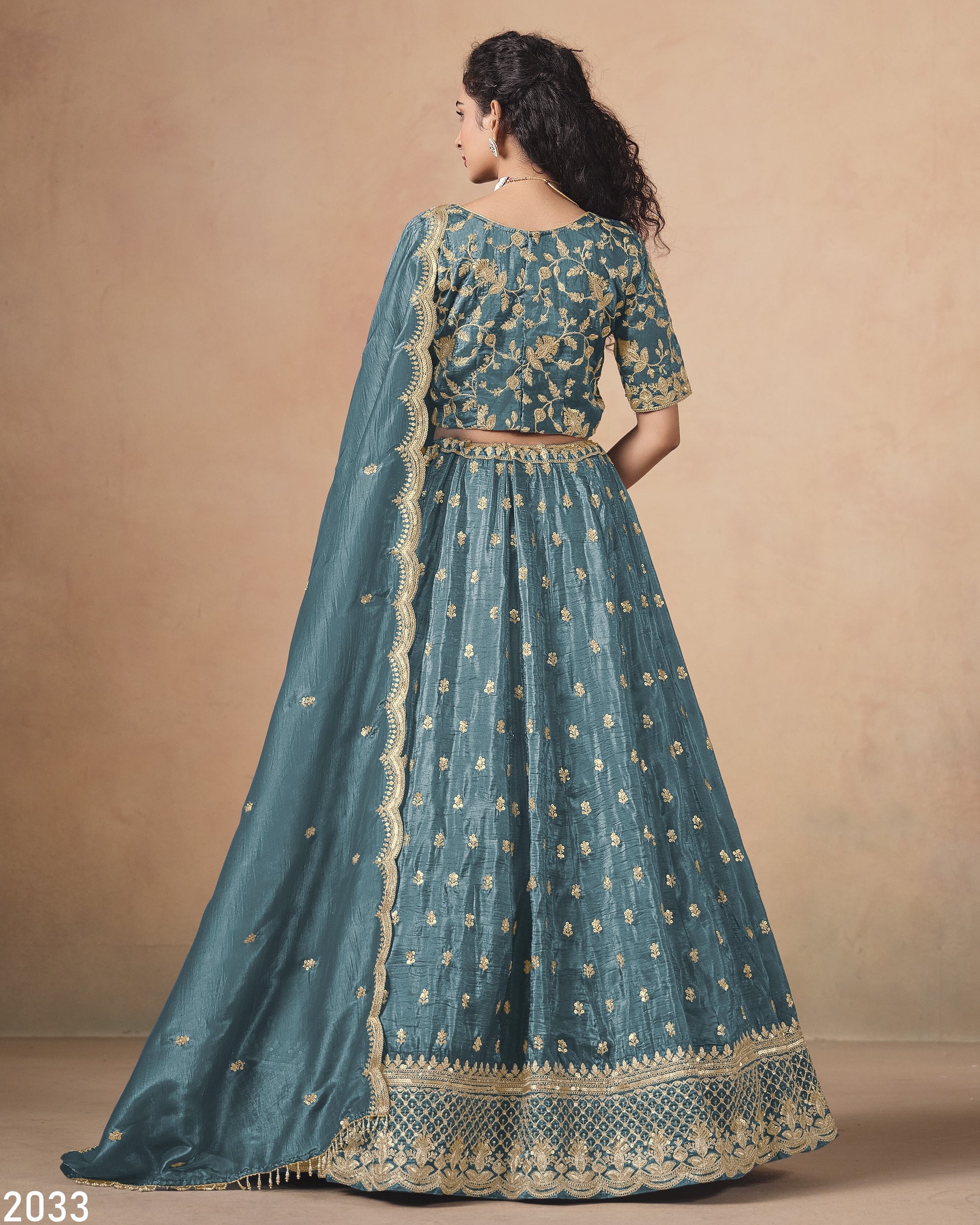 Teal embroidered traditional outfit with gold details on a beige background