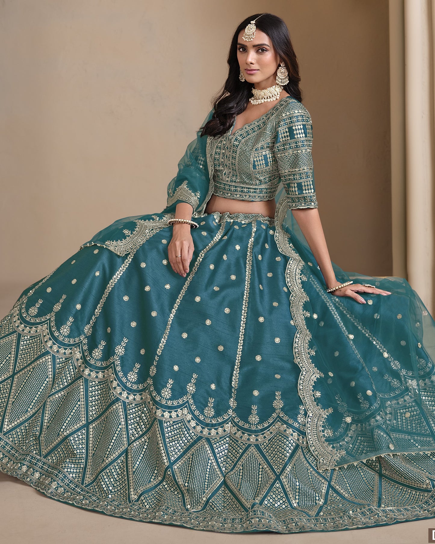 Woman wearing a teal embroidered traditional outfit with a beige background