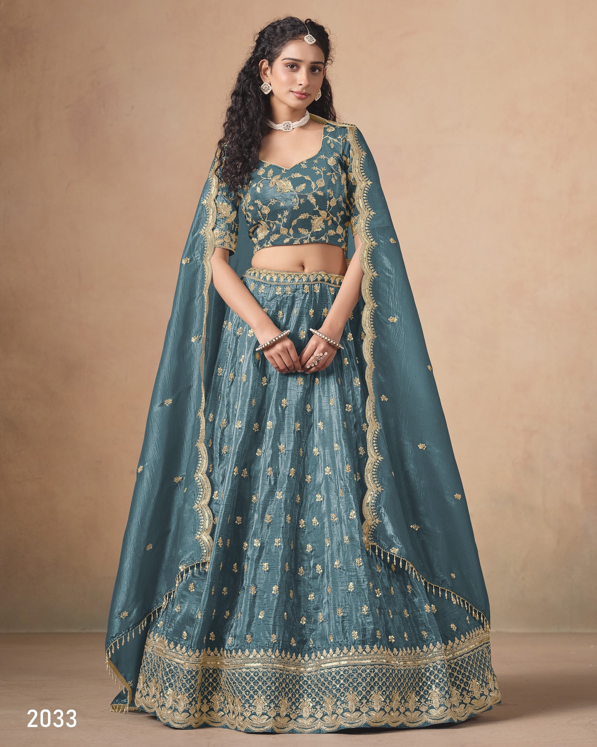 Woman wearing a teal embroidered lehenga with gold details against a beige background