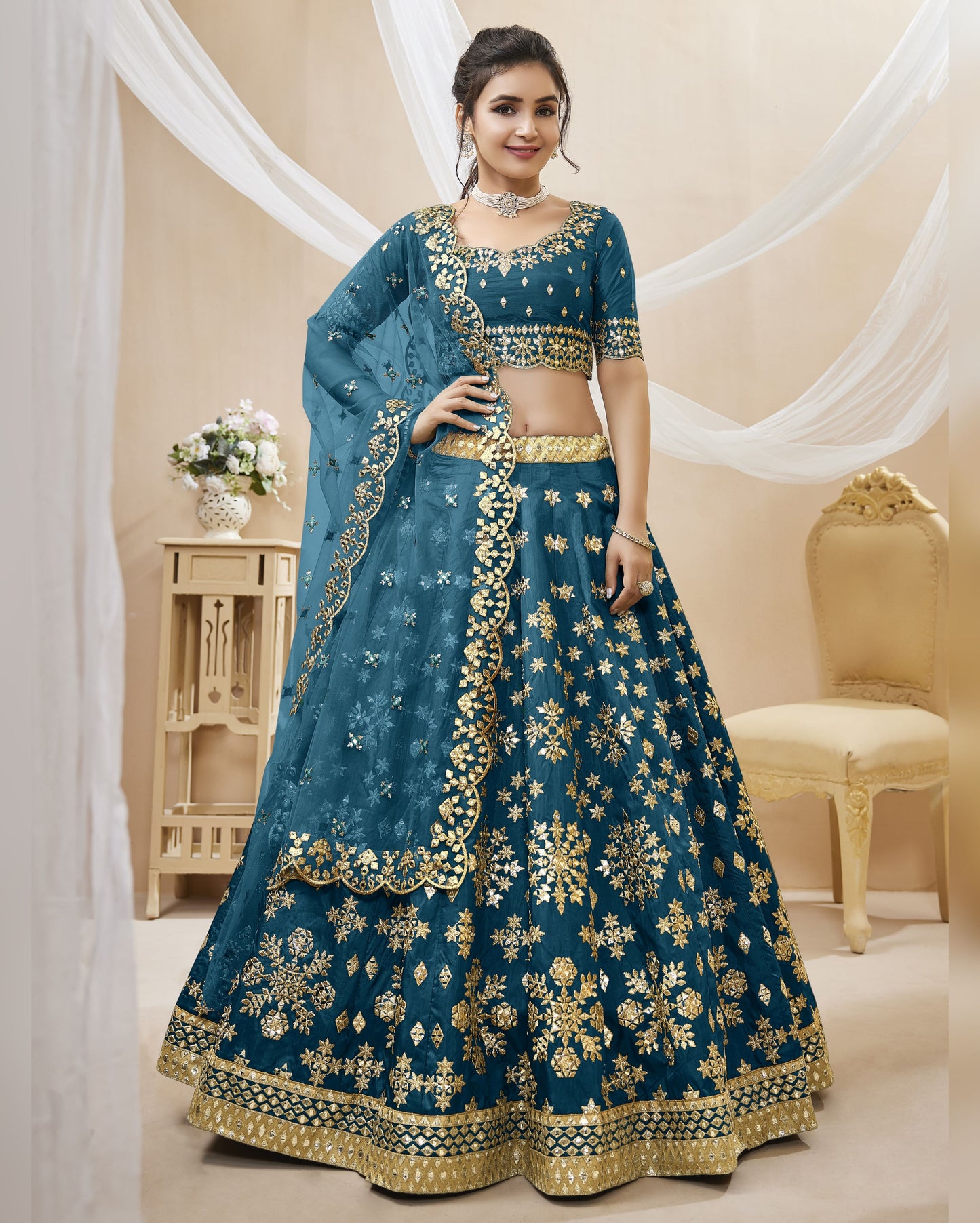 Woman wearing a blue embroidered traditional outfit with gold details in a decorated room.