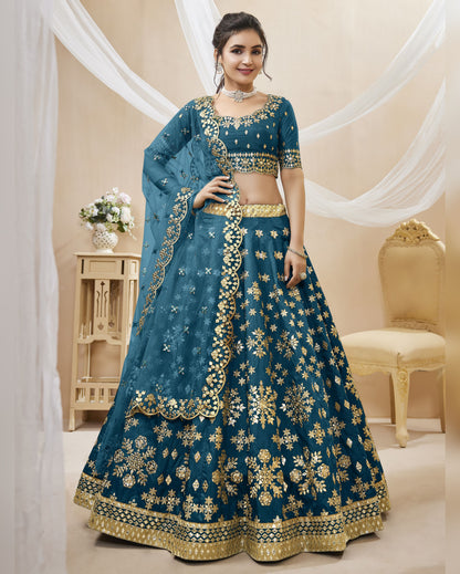 Woman wearing a blue embroidered traditional outfit with gold details in a decorated room.