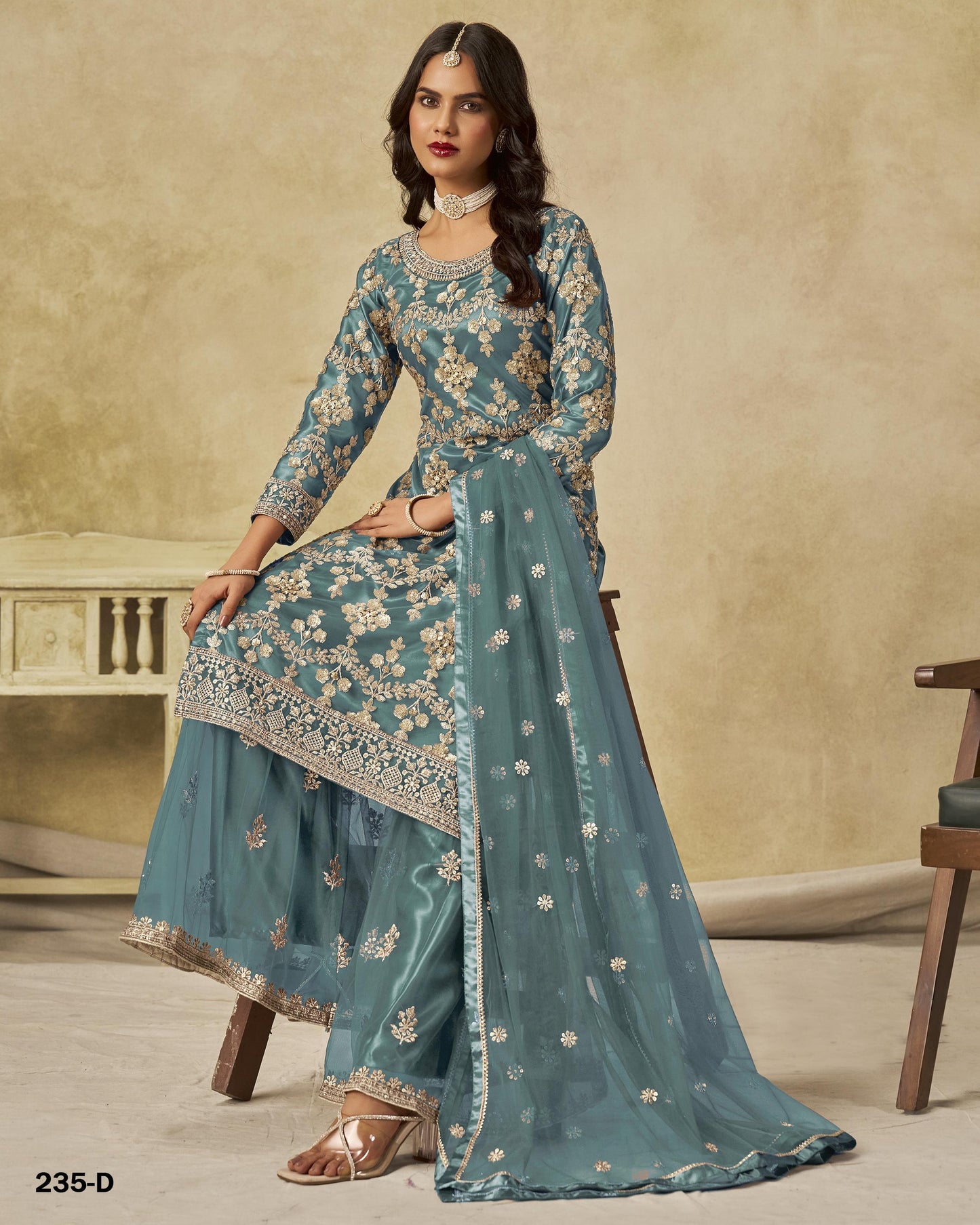 Woman wearing a teal embroidered traditional outfit with a beige background