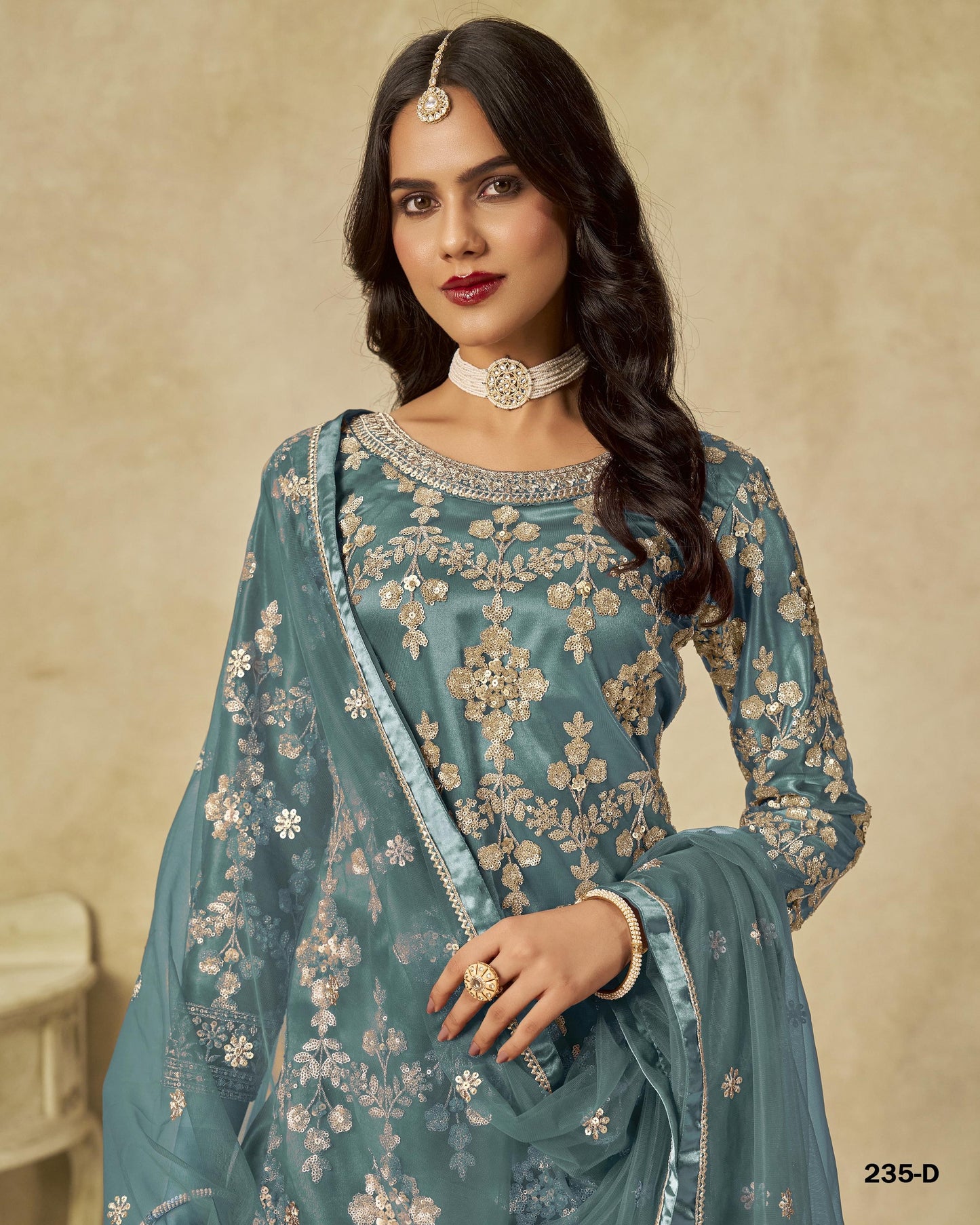 Woman wearing a teal embroidered traditional outfit with a beige background