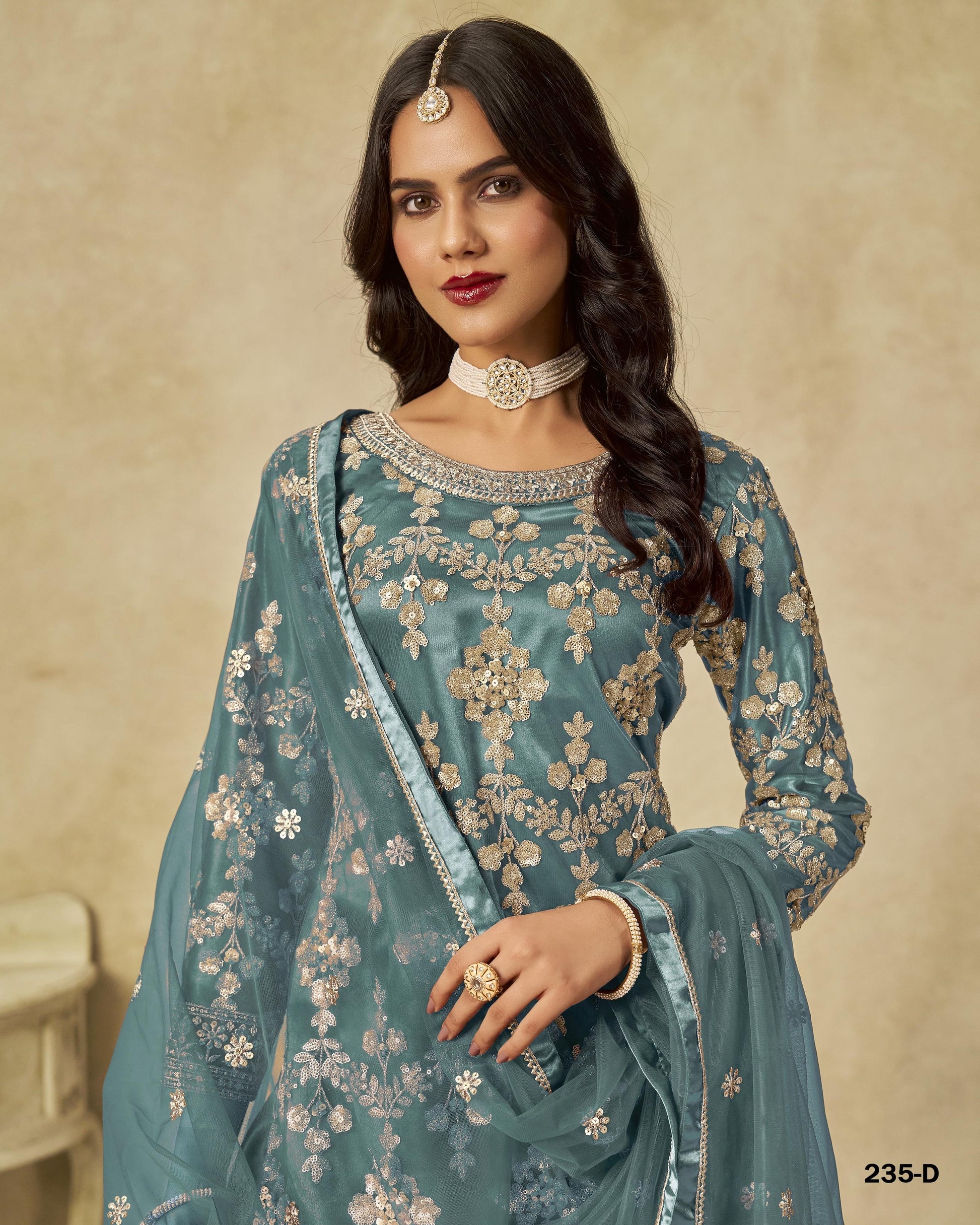 Woman wearing a teal embroidered traditional outfit with a beige background