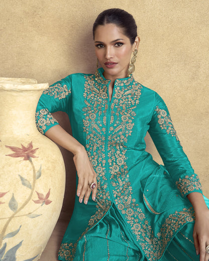 Woman wearing a teal embroidered traditional outfit against a beige background