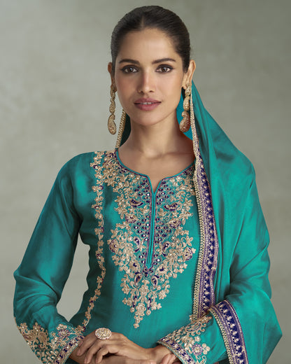 Woman wearing a teal embroidered traditional outfit with a plain background