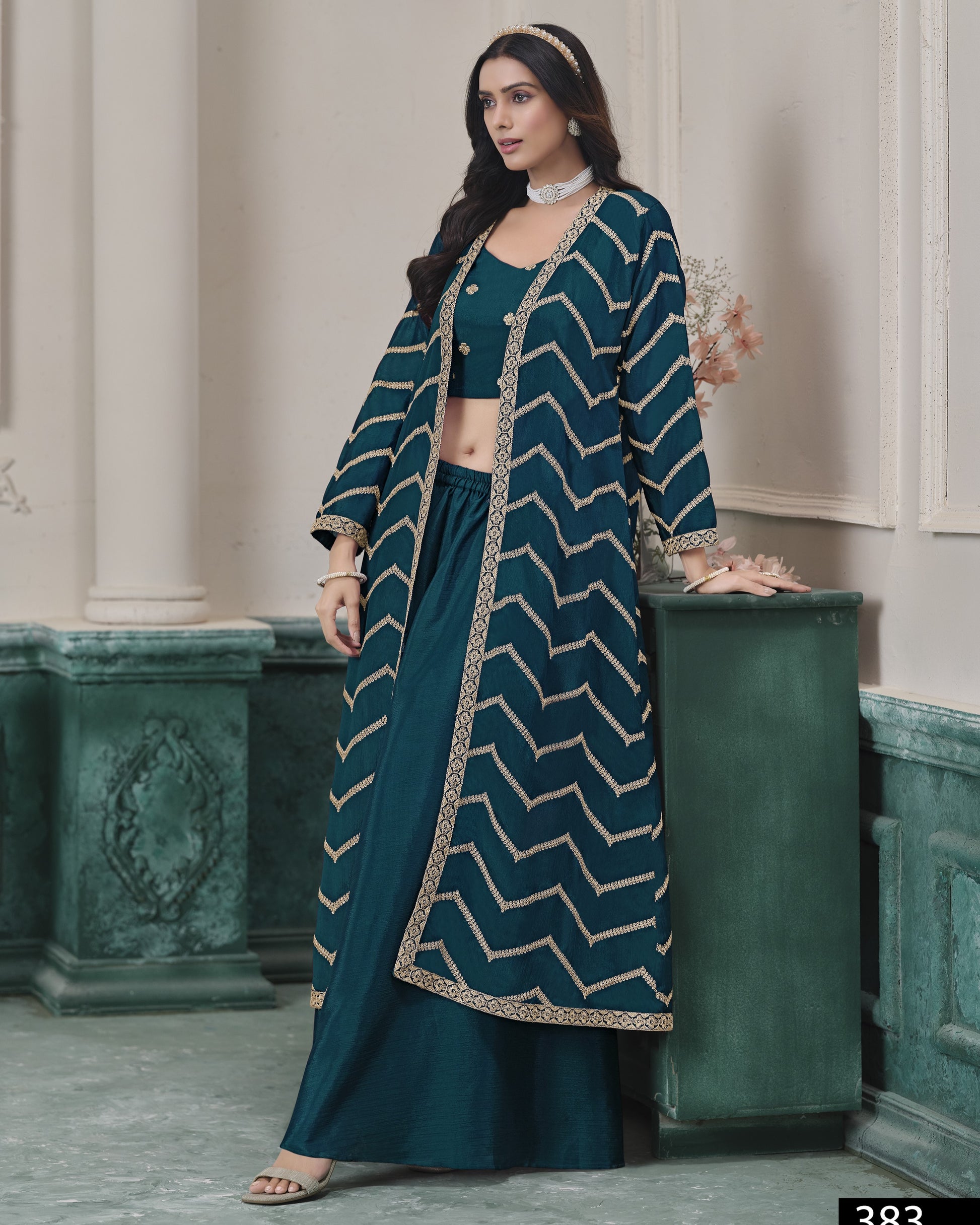 Woman wearing a teal outfit with a patterned jacket in an elegant interior setting.