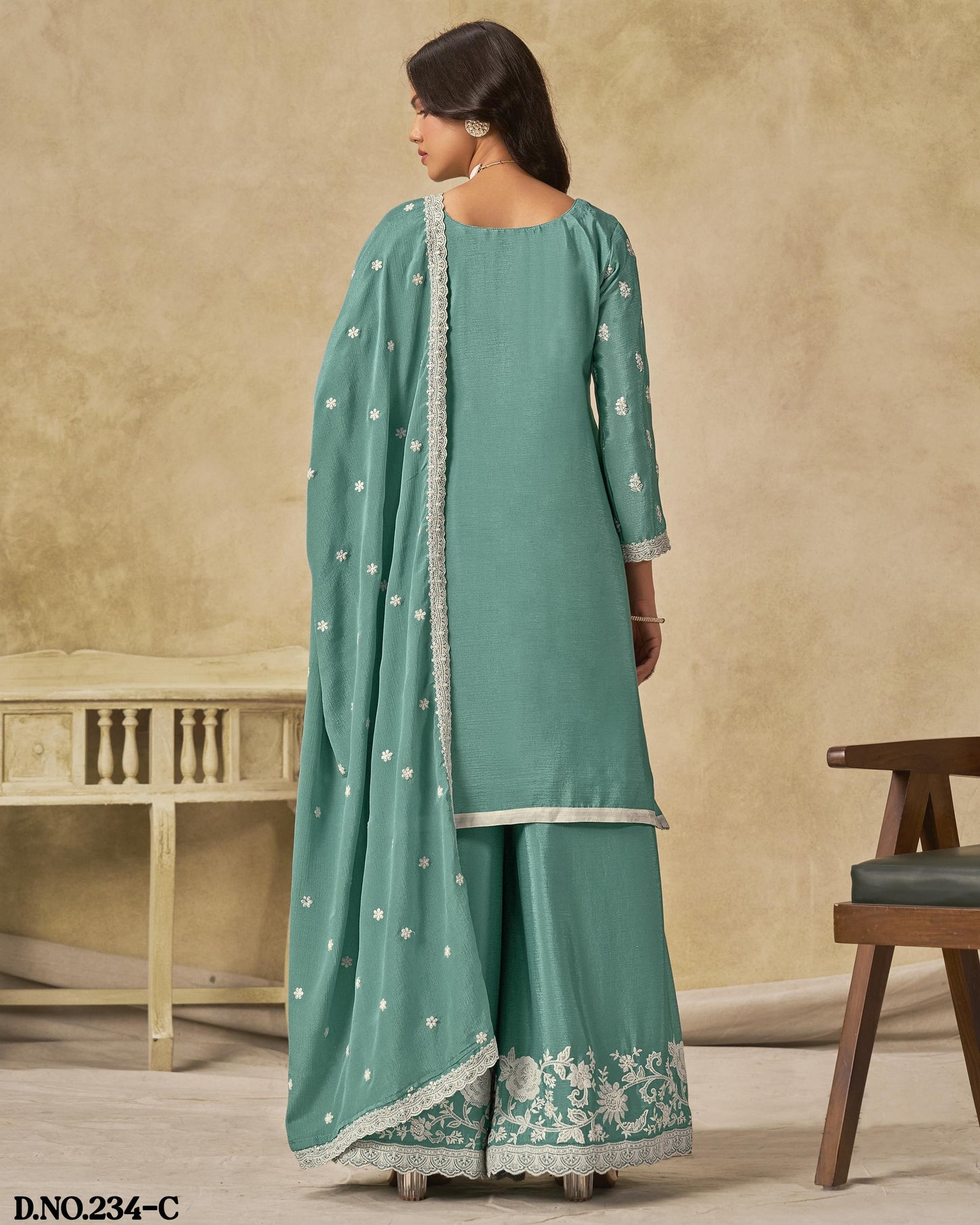 Woman wearing a teal traditional outfit with white patterns in a neutral setting