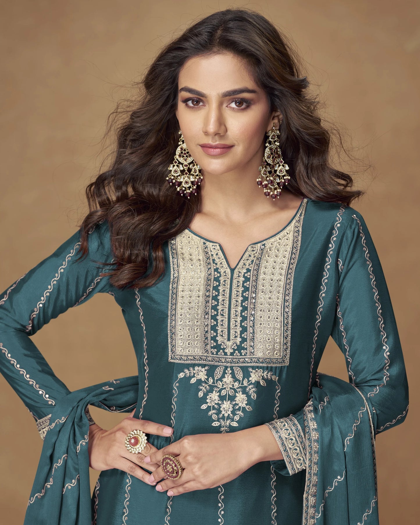 Woman wearing a teal embroidered outfit with jewelry on a brown background