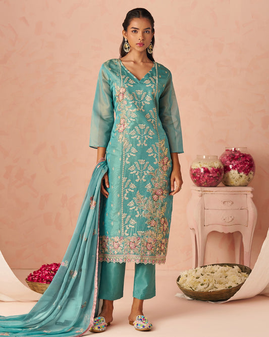 Woman wearing a teal embroidered outfit with a matching dupatta on a pink background