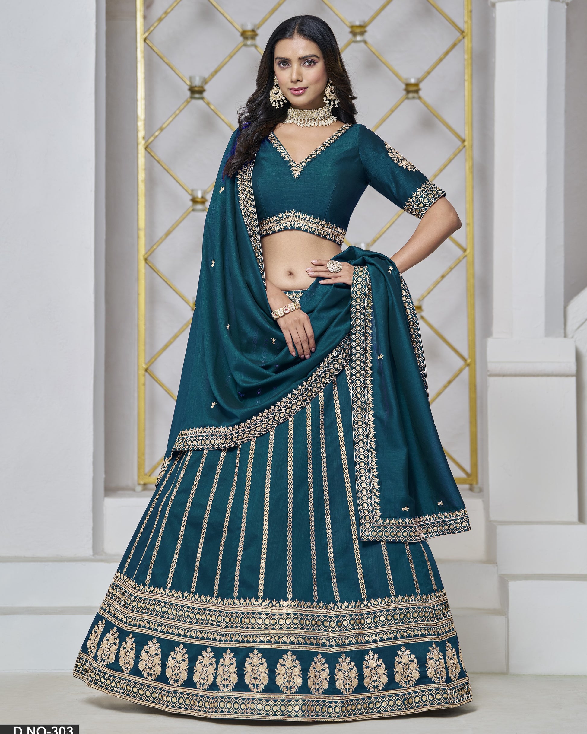 Teal lehenga with gold embroidery worn by a model against a decorative wall.