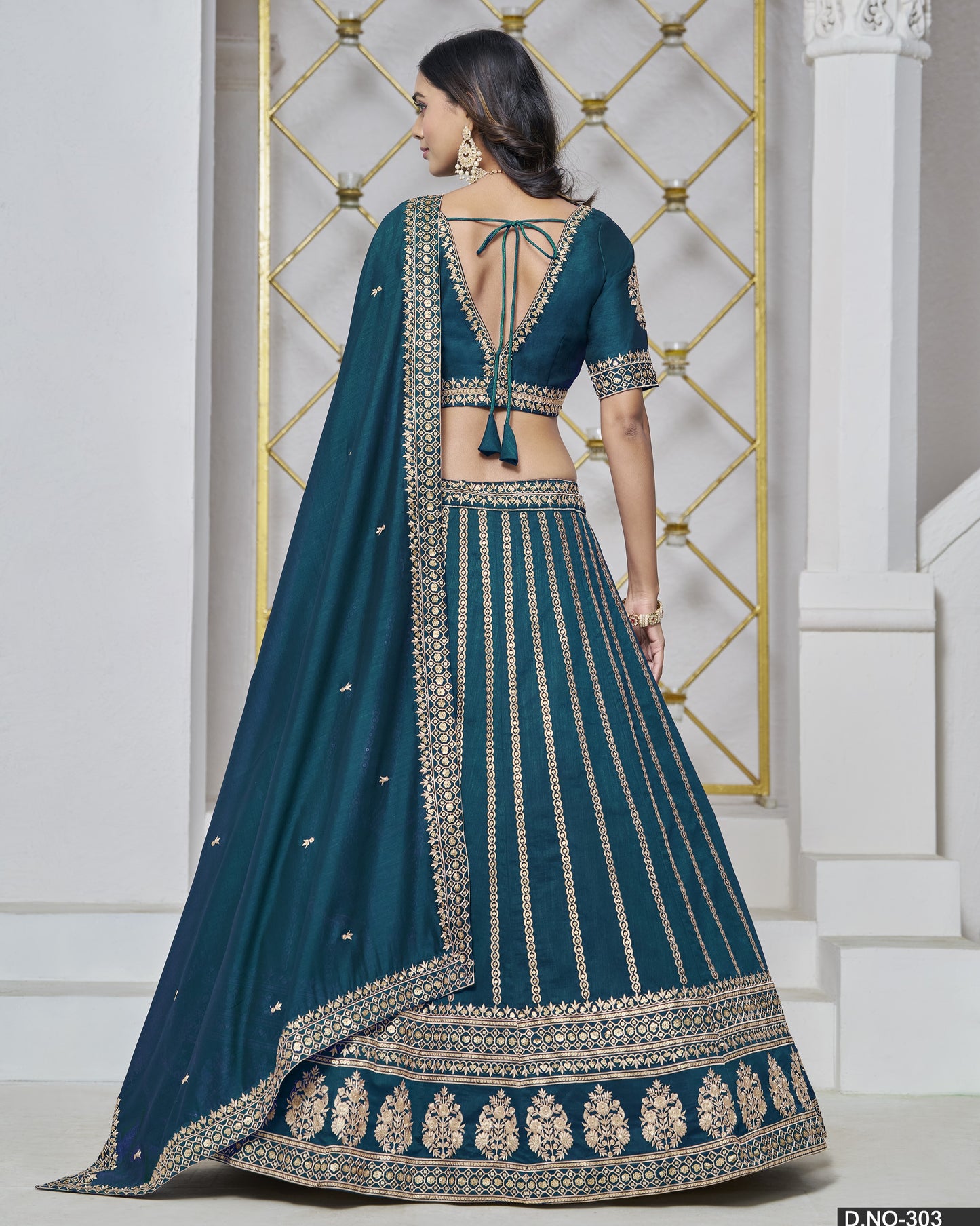 Teal lehenga with intricate embroidery in front of a decorative wall.