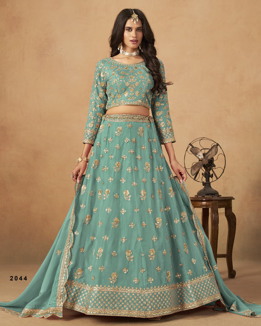 Woman wearing a teal embroidered lehenga with a beige background