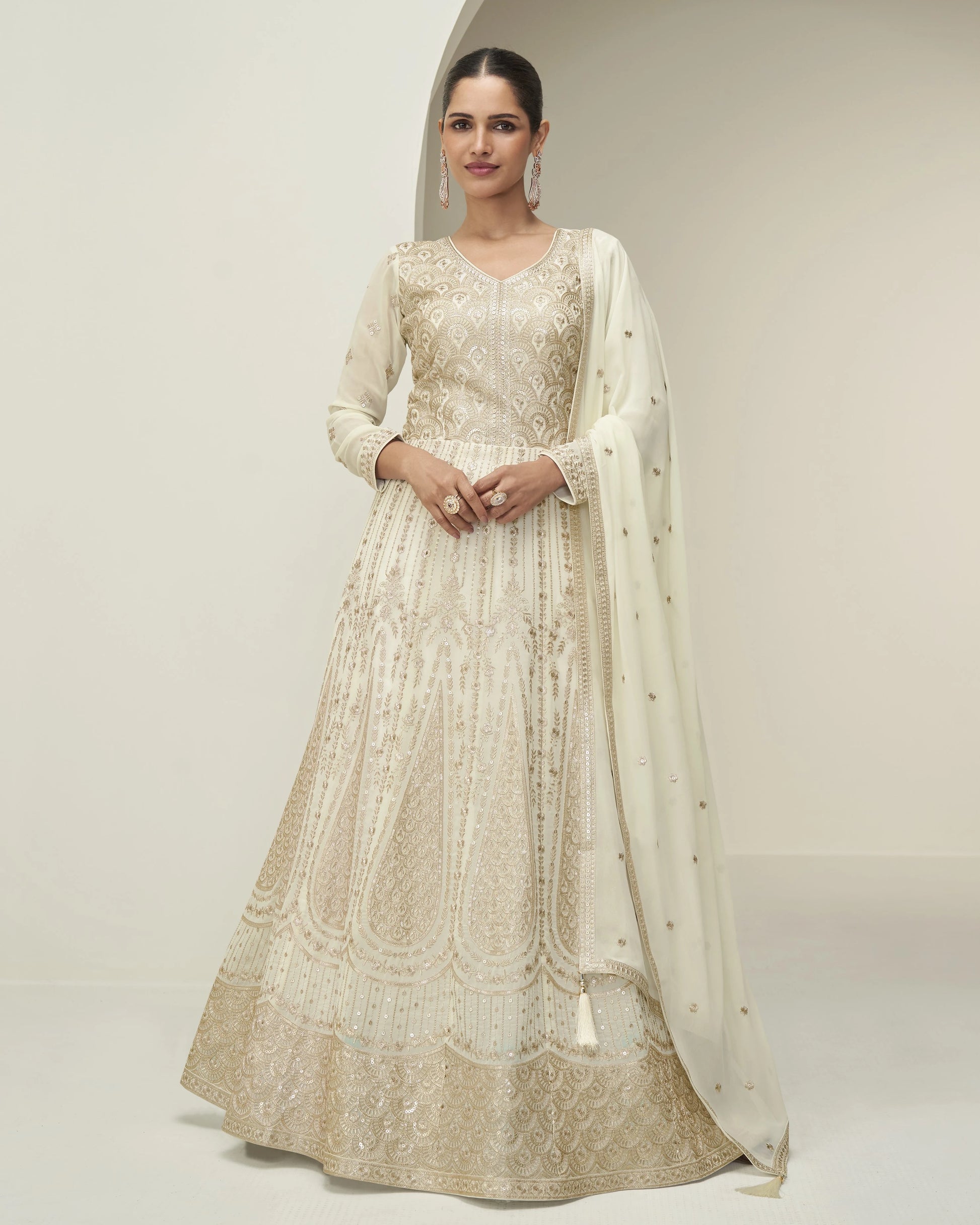 Woman wearing a beige embroidered anarkali suit with a matching dupatta on a plain background
