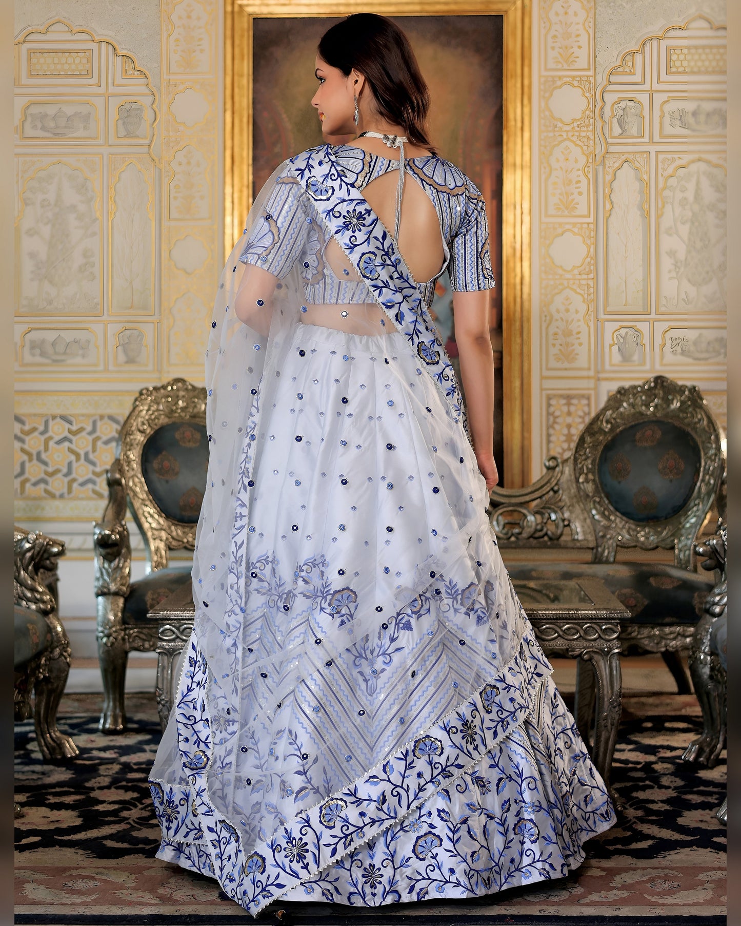 Woman in a white and blue embroidered traditional outfit standing in an ornate room.