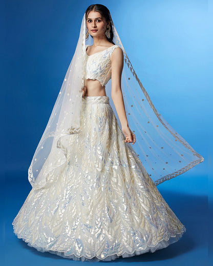 Woman wearing a white embroidered lehenga with a matching dupatta against a blue background