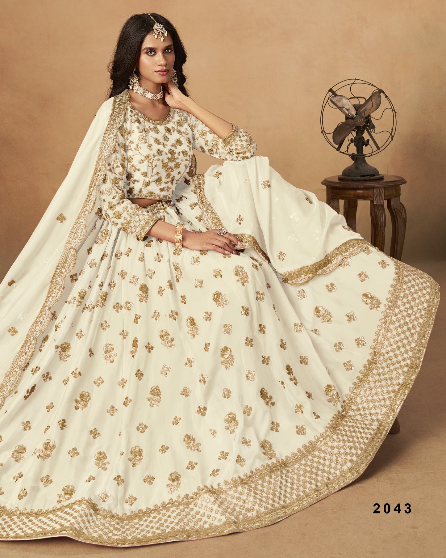 Woman in a white and gold embroidered traditional outfit sitting on a brown background