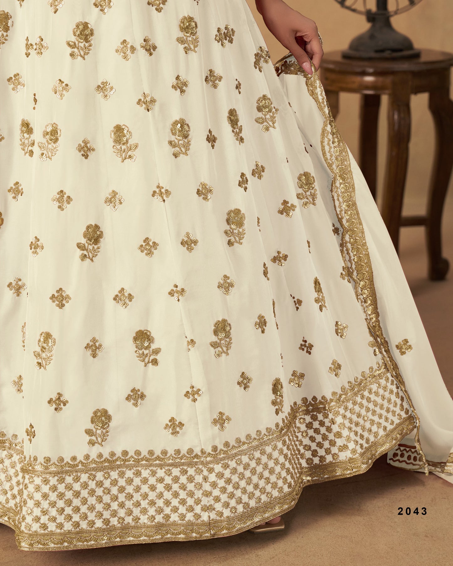 Close-up of a cream-colored fabric with gold embroidery on a wooden floor.