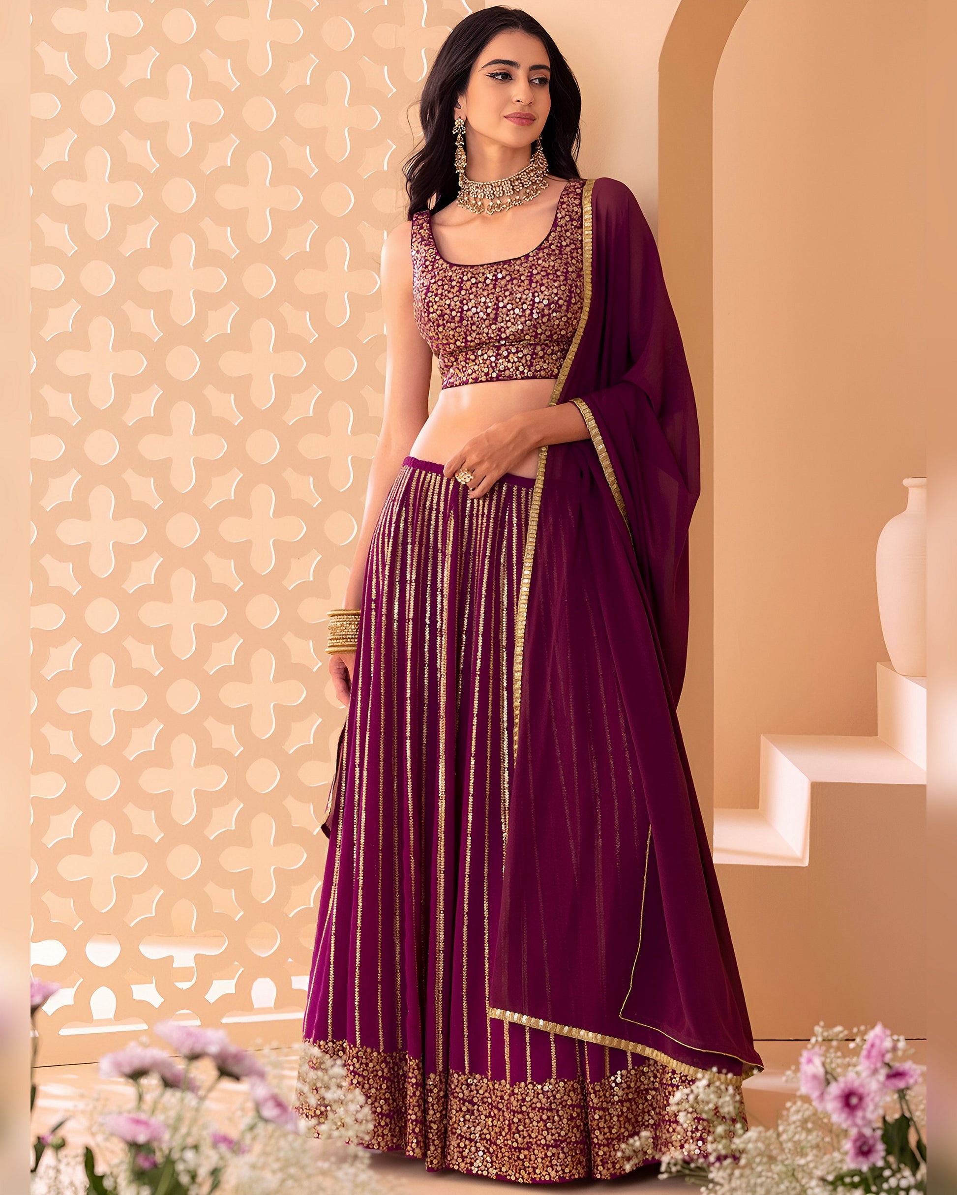 Woman in a purple traditional outfit with gold details against a decorative wall.