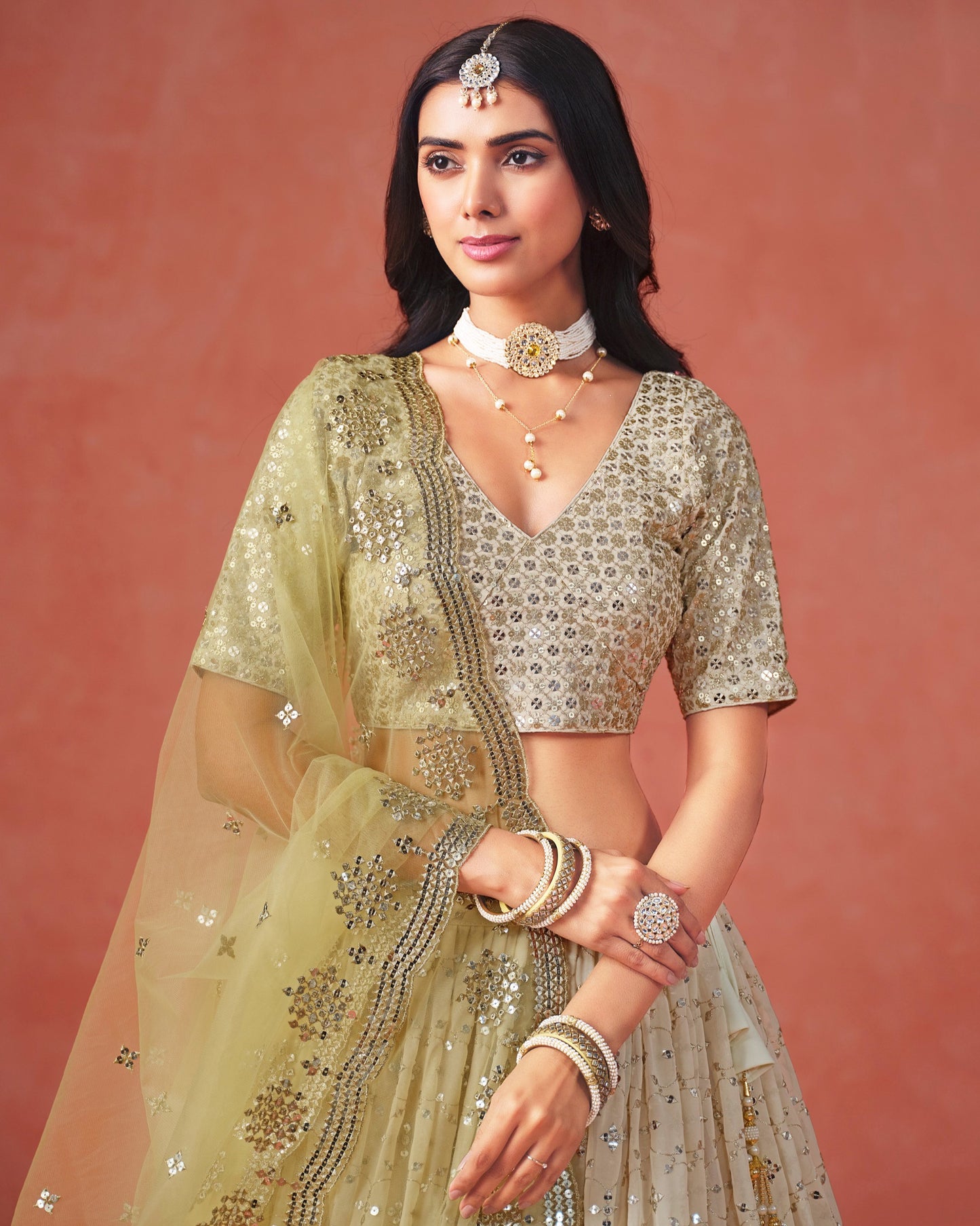 Woman in traditional embroidered outfit with jewelry against a pink background
