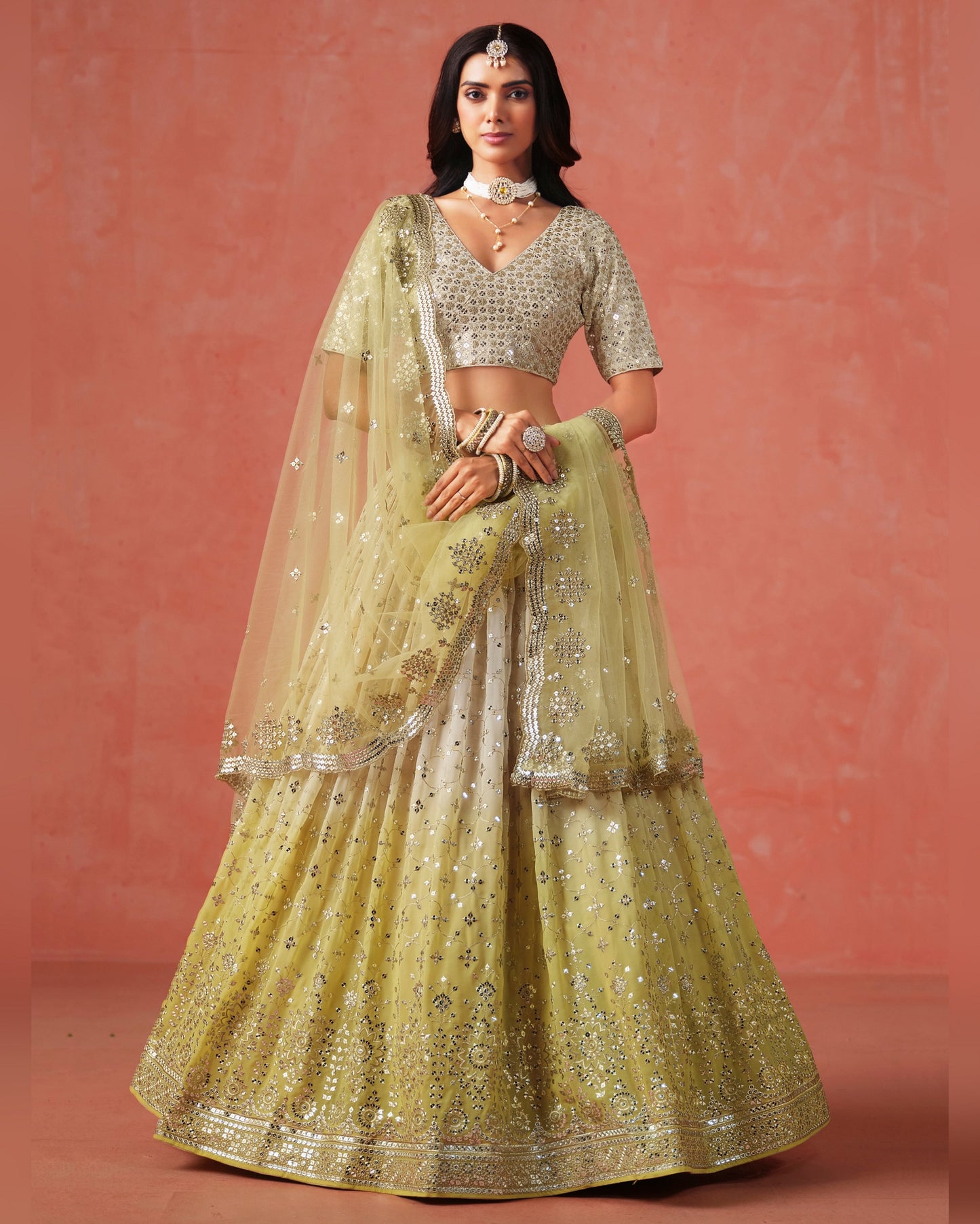 Woman wearing a traditional yellow embroidered lehenga with a matching blouse against a pink background
