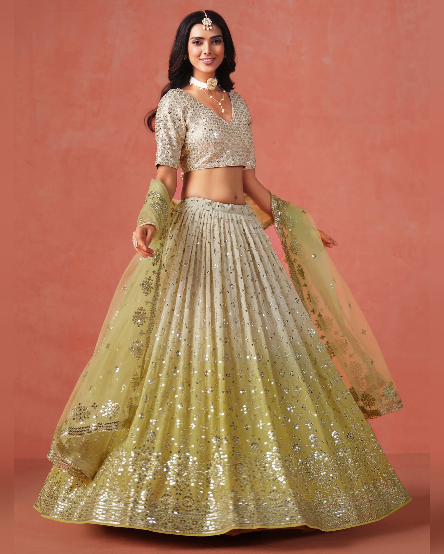 Woman wearing a traditional outfit with a gold and silver lehenga on a pink background